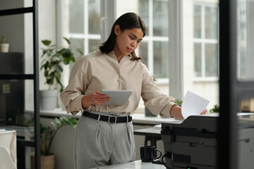 Fototapete - Young confident female office worker in elegant attire printing paper documents on xerox machine and using tablet against window