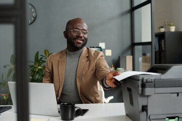 Fototapete - Young successful white collar worker taking printed financial document from tray of xerox machine while preparing contract before negotiation