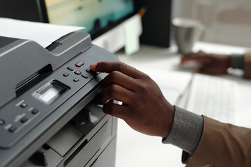 Fototapete - Hand of young African American male office worker pressing button on panel of xerox machine while starting making copies of documents