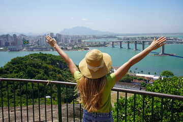 Wall Mural - Joyful girl visiting Brazil. Beautiful young woman with raised arms enjoying view of Vitoria cityscape the capital of Espirito Santo state in Brazil.