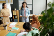 © pressmaster - Clever schoolgirl in denim casualwear explaining new grammar rules to classmates during presentation while standing next to teacher