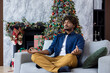 © Liubomir - Christmas young man meditating in lotus pose sitting on sofa in living room, hispanic man doing breathing exercises calm down and relaxing new year celebration.