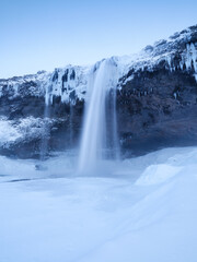 Wall Mural - Seljalandsfoss waterfall, Iceland. Icelandic winter landscape.  High waterfall and rocks. Snow and ice. Powerful stream of water from the cliff. A popular place to travel in Iceland.