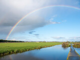 Fototapeta Tęcza - canal between dutch meadows in holland near utrecht with rainbow in blue sky
