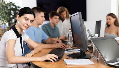 Wall Mural - Portrait of interested motivated young female software developer working in IT startup, sitting at computer desk and coding with group of coworkers