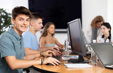 Wall Mural - Cheerful interested young guy using computer to surf internet in student library, searching educational resources and materials during self-study..