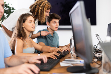 Enthusiastic young girl studying in computer lab with fellow students engrossed in coursework. Digital education concept..