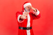 Santa claus in red costume pinching nose with fingers to avoid bad smell and showing stop gesture, demonstrating repulsion to stink, awful odor. Indoor studio shot isolated on red background.
