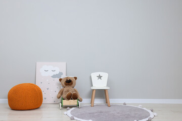 Sticker - Kindergarten interior. Small chair, toy, ottoman and picture near grey wall, space for text