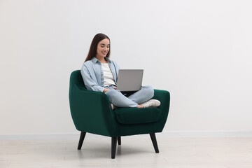 Canvas Print - Beautiful woman using laptop while sitting in armchair near white wall indoors