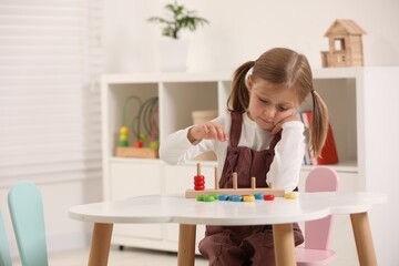 Wall Mural - Cute little girl playing with stacking and counting game at white table indoors, space for text. Child's toy