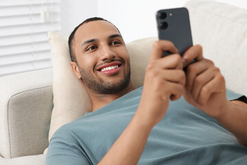 Wall Mural - Happy man sending message via smartphone indoors