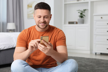 Wall Mural - Handsome man sending message via smartphone at home. Space for text