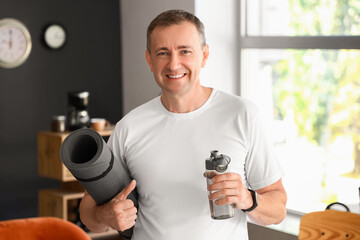 Poster - Sporty mature man with bottle of water and fitness mat at home