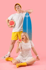 Canvas Print - Young man with woman holding fresh watermelon and surfboard on pink background