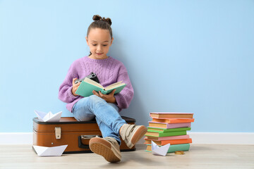 Sticker - Cute little girl with photo camera reading adventure book near blue wall