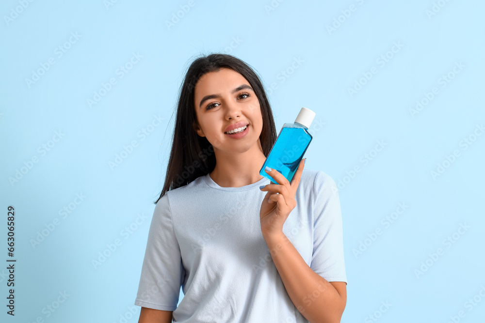 Smiling young woman with mouth rinse on blue background