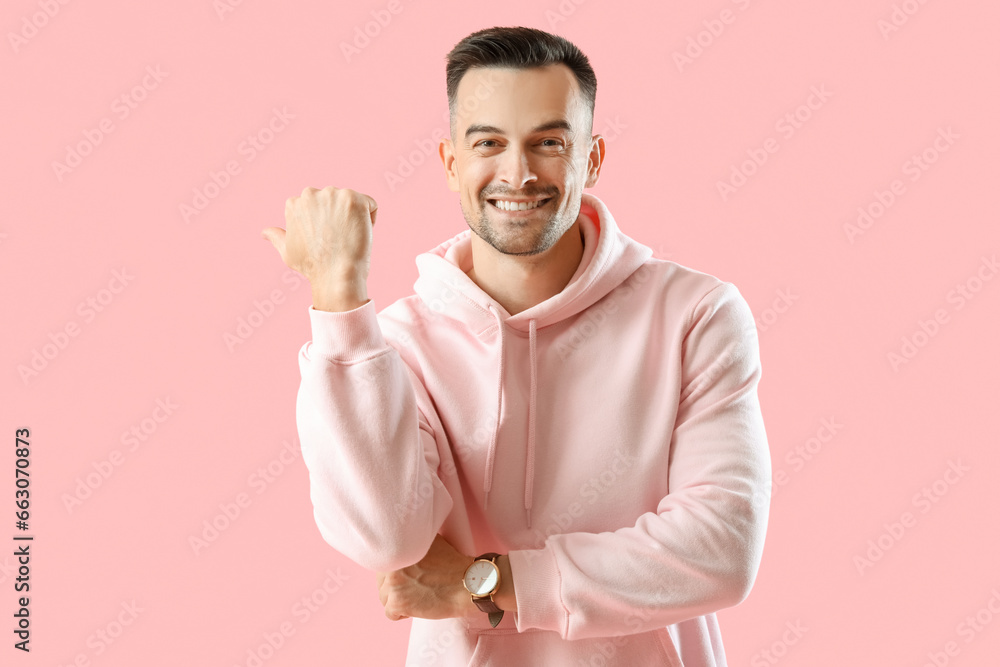 Happy young man pointing at something on pink background