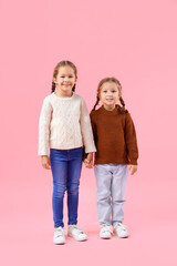 Wall Mural - Cute little girls in warm sweaters holding hands on pink background