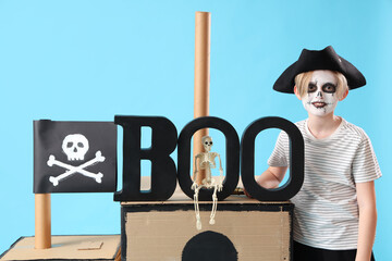 Wall Mural - Little boy dressed for Halloween as pirate with cardboard ship on blue background