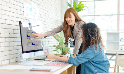 Asian professional successful young female creative graphic designer and colleague in casual fashion suit smiling helping choosing sampling comparing artwork on computer moniter in office workplace