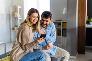 Wall Mural - Smiling couple embracing while looking at smartphone. People sharing social media on smart phone.