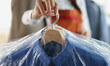 © H_Ko - Close-up of worker giving to client clean clothes hanging on hangers at dry cleaning company. Garment packed in plastic bags. Dry cleaning service concept