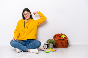 Wall Mural - Young Chinese student woman sitting on the floor isolated on white wall doing strong gesture