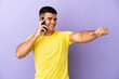 © luismolinero - Young handsome man using mobile phone over isolated purple background giving a thumbs up gesture