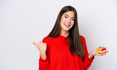 Wall Mural - Young Brazilian woman holding a tartlet isolated on white background pointing to the side to present a product