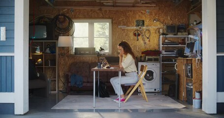 Hispanic Female Software Engineer Coding On Laptop Computer In Garage At Home. Focused Young Woman Working On Innovative Online Service Startup Company. Digital Entrepreneur Starting Business Concept.