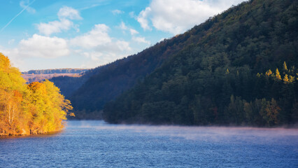 Wall Mural - countryside scenery by lake in fall season. scenery with forested mountains in vivid autumn colors. 