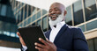 © N Felix/peopleimages.com - Tablet, smile and senior businessman in the city doing research for a legal strategy. Happy, digital technology and elderly professional African male lawyer working on case commuting in urban town.
