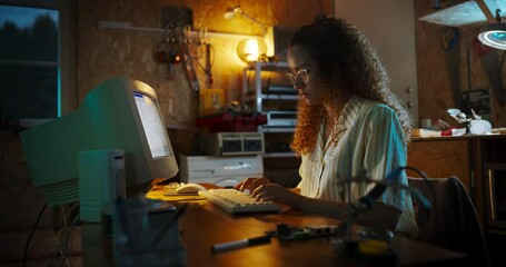 Fototapete - Hispanic Female Engineer Using Old Desktop Computer In Nineties Retro Garage In The Evening. Intelligent Woman Programming, Working On Innovative Portable Device, Starting Technological Company.