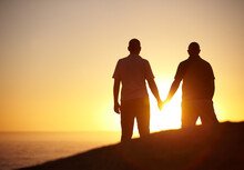 Silhouette, Sunset And A Gay Couple At The Beach Holding Hands For Bonding, Love And A Date. Back, Dark And Lgbtq Men With Care, Support And Watching The View At The Ocean Or Sun On A Vacation