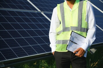 Wall Mural - Male arab engineer standing on field with rows of solar panels.