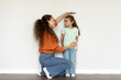© Home-stock - Young european mother measuring height of her daughter near white wall at home, full length shot