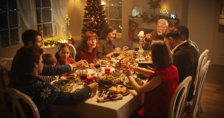 Wall Mural - Diverse Group of People, Young and Old, Share a Joyful Christmas Dinner at Home. Family Sitting Behind a Big Dining Table Full of Delicious Food with Roast Turkey Feast. High Angle Evening