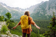 Smiling traveler with a bright backpack on a hiking mountain trail. A beautiful woman on a cliff enjoying the mountain scenery. Active lifestyle.