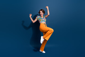 Poster - Full body photo of pretty young girl raise fists celebrate winning wear trendy flared pants outfit isolated on dark blue color background