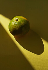 Wall Mural - A tangerine on a yellow background. Still life fruit photo with shadow and light