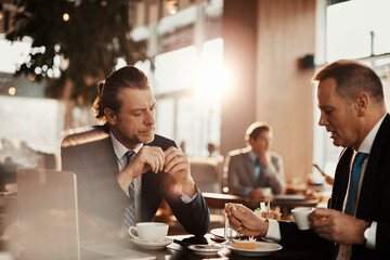 Wall Mural - Two Caucasian middle aged businessmen having a meeting over some coffee in a café decorated for Christmas and the new year holidays