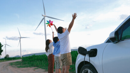 Sticker - Concept of progressive happy family enjoying their time at wind farm with electric vehicle. Electric vehicle driven by clean renewable energy from wind turbine generator for charging station.