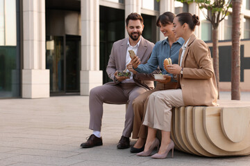 Business lunch. Happy colleagues spending time together during break on bench outdoors