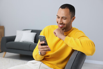 Wall Mural - Happy man sending message via smartphone indoors