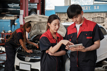 Two Asian professional mechanics, male supervisor engineer, and partner discuss and inspect repair work checklists at garage, service car maintenance, and fixing specialist occupations auto industry.