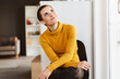 © contrastwerkstatt - Young Modern Woman with Short Hair and Yellow Sweater Sitting in Office Chair, Smiling Upward
