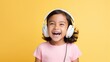 A little girl with headphones listens to music expressing real emotions against yellow background.