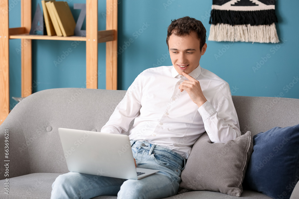 Young man with laptop sitting on sofa at home