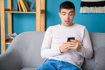 Sticker - Surprised young man with smartphone sitting on sofa